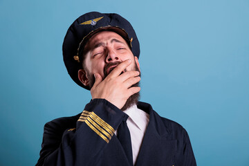 Tired airplane aviator yawning closeup, exhausted pilot covering open mouth with hand. Sleepy aviation academy aircraft captain in aviation uniform with closed eyes front close view © DC Studio