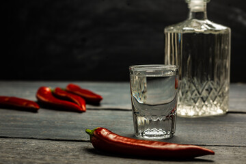 Ukrainian gorilka or vodka or rum or tequila (transparent highly alcoholic drink) in jar and shot. with red pepper on dark background. - obrazy, fototapety, plakaty