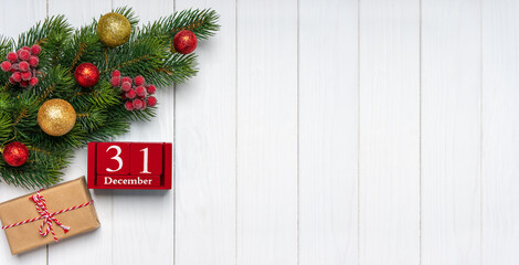 Fototapeta na wymiar Christmas tree branch with decor, gift box and red perpetual calendar with date 31 december on white wooden background. Top view, flat lay with copy space, banner, header, New Year background