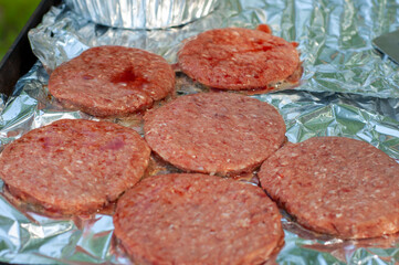 Raw hamburger on aluminum foil on grill cooking