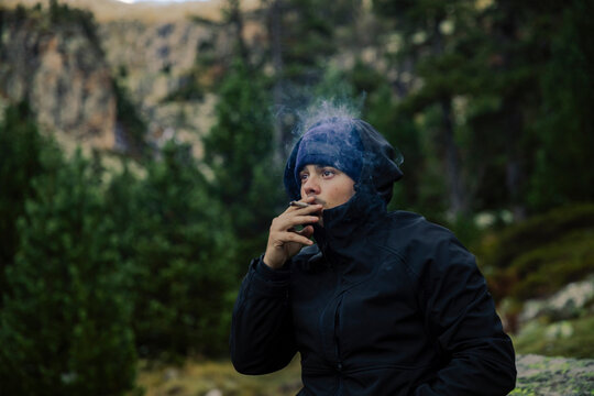 Boy with coat and hat smoking a marijuana cigarette in nature