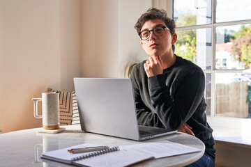 Fototapeta premium man thinks and touches chin at table with laptop