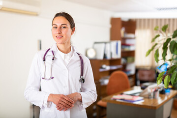 Portrait of a positive young female therapist standing in a well-lit clinic office. Close-up portrait