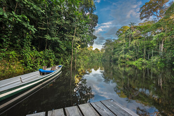 Low point of view on the Cuyabeno amazonian river with blue sky, reflection in the water, pontoon...