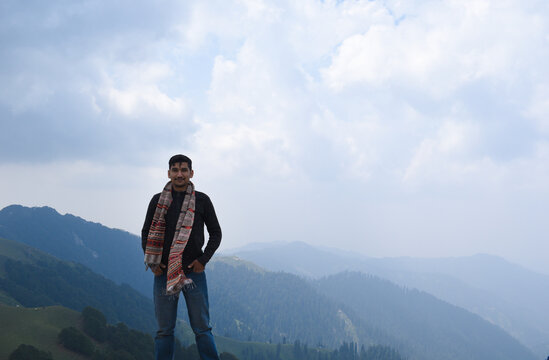Indian guy standing top of mountain wearing pahadi himachali muffler. Beautiful mountain valley in background