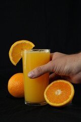 Hand picking up glass of orange juice on black background © srkalamari