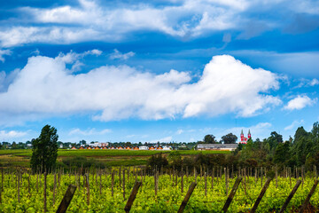 Paisaje del pueblo la ciudad de Cauquenes de Chile, debajo de un cielo con muchas nubes luego de la lluvia, mucho césped y arboles en primer plano con la iglesia roja a la vista