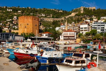 Fototapeta na wymiar Pier of Alanya with moored boats. View of Kizil Kule (Red Tower) and Castle of Alanya, Antalya Province, Turkey.