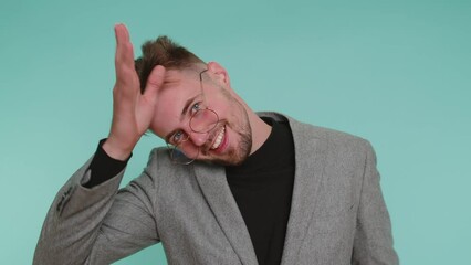 Funny joyful sincere business man 20 years old in jacket making playful silly facial expressions and grimacing, fooling around showing tongue. Young handsome guy isolated alone on blue wall background