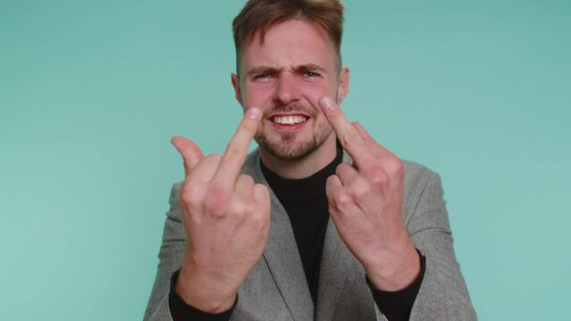 Aggressive crazy hooligan business man showing around his middle finger, demonstrating protest with impolite rude gesture of disrespect, rejecting communication. Young guy isolated on blue background