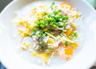 Top view and close up. Hot rice porridge in bowl sprinkled with onions Ginger chopped into small strips Fried Wontons and soft-boiled egg.