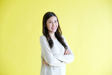 Happy asian woman smiling, arm cross and looking at camera while standing over isolated yellow background, Portrait of asia female