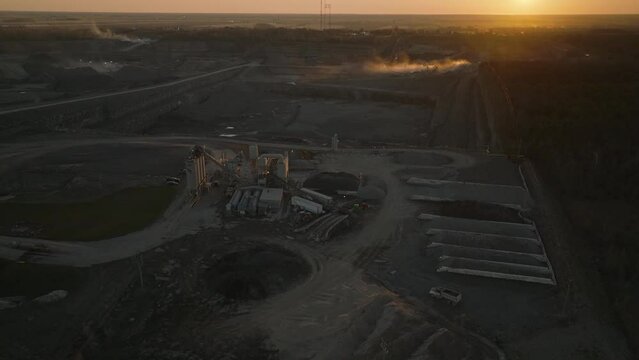 Reversing cinematic drone shot of a stone quarry at dusk with stockpiles and concrete equipment in foreground