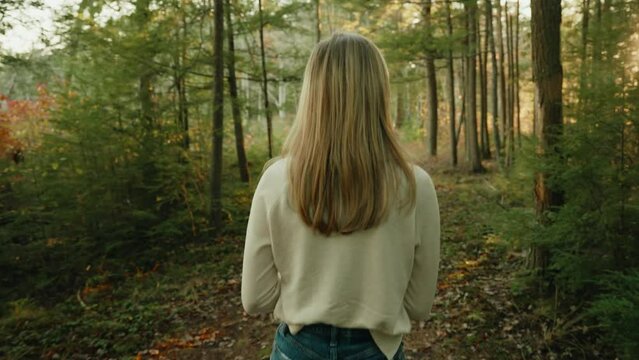 White shirt blond girl walking though the forest during sunset