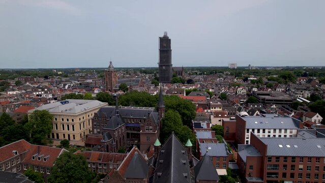 Descending aerial showing De Dom medieval cathedral tower in scaffolding in Dutch city center of Utrecht towering over the cityscape at sunrise revealing a church in the foreground