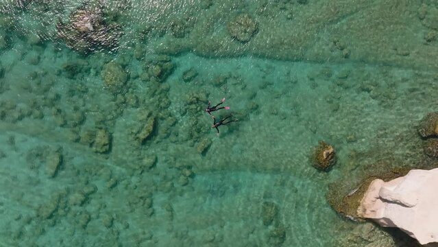 Drone riser - snorkeling couple holds hands in clear blue shallows float on back