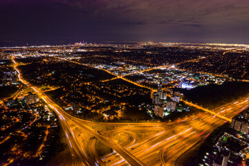 Fototapeta premium Top view of car traffic at intersection lane and buildings. Long exposure of urban cityscape at night. Modern city in Canada full of night lights from energy and power.
