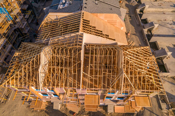 Modern North American home in construction. Aerial view of unfinished city house with wooden roof ribs frame structure. Roof beams under construction.