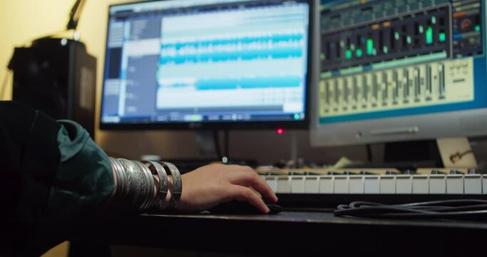 Woman's arm with bracelets controls a digital audio workstation in a recording studio with a mouse.