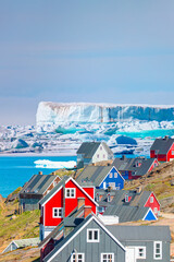 Picturesque village on coast of Greenland a giant iceberg in the background - Colorful houses in Tasiilaq, East Greenland