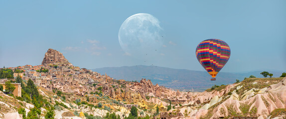 Hot air balloon flying over rock landscape at Cappadocia with full moon - Goreme, Turkey 