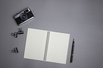 Black and white office theme with camera, pen and notebook over the grey background. 