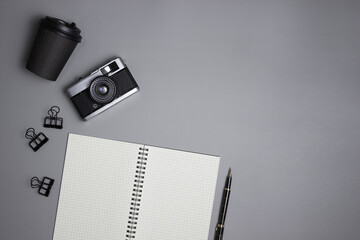 White notebook with camera and a cup of coffee on grey background with copy space.