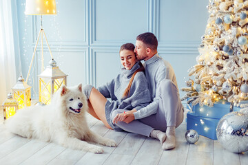 happy couple with a dog sitting near Christmas tree at home. hearth, home clothes and sweaters
