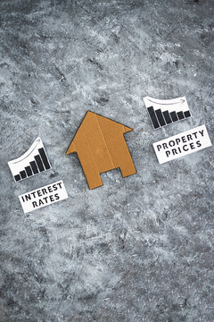 interest rates increasing and property prices dropping, cardboard house in between graphs with stats going in opposite directions