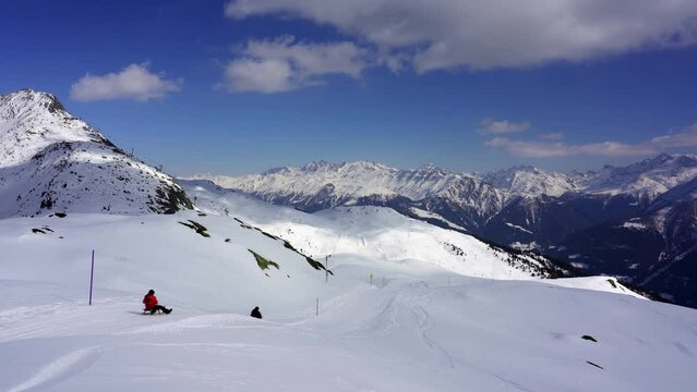 Aletsch Arena winter ski resort, happy tourists slide down a piste on a sledge in the snow capped mountains of the alps, Switzerland