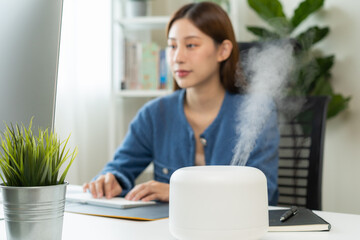 Modern air humidifier device during sitting workplace, happy asian young woman using computer work...