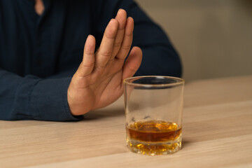 Alcoholism, depressed asian young man refuse, push out alcoholic beverage glass, drink whiskey, sitting alone at night. Treatment of alcohol addiction, having suffer abuse problem alcoholism concept.