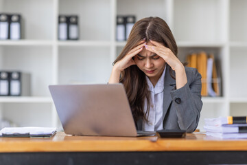 Young business Asian woman stressed while working, Tired asian businesswoman with headache at home office, payment stressed and confused by calculate expense from invoice or bill tax.
