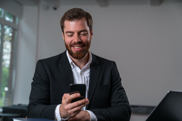 Smiling handsome businessman wearing formal suit is watching at smartphone