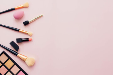 Makeup brushes and sponges used to apply makeup flat lay with space for words on pink background
