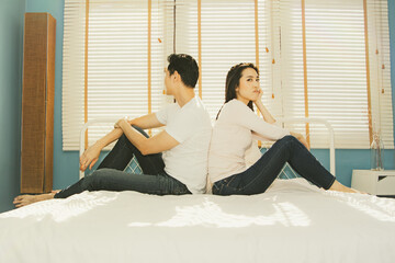 Asian couple sitting in bedroom angry and upset sulking at each other with serious grimace sit with...