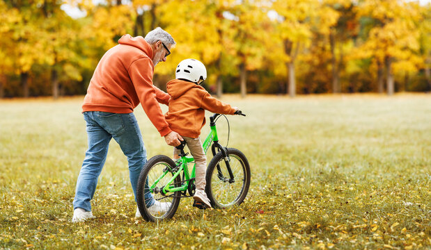 Happy family grandfather teaches child grandson  to ride a bike in park