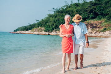 Happy senior couple using smart phone together on the beach having fun in a sunny day, activity after retirement in vacations and summer.