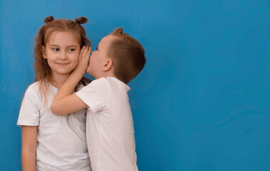 Little boy whispers in girl's ear telling her something secret, good news on blue background with...