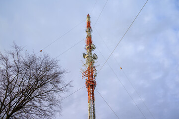 Broadcast and 5G mobile cell tower against the sky with tree in lower corner