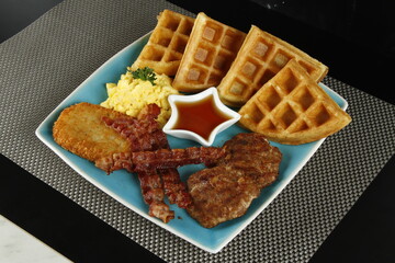 Breakfast platter with bacon, hash brown, beef burger patty, scrambled egg and waffles