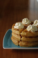 Side shot of waffle stack with whipped butter, wood table, dramatic lighting