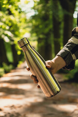 Close-up of Unrecognizable female hand holding Water bottle. Reusable steel thermo water bottle in...