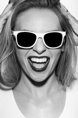 Fashion, make-up and lifestyle concept. Beautiful woman close-up studio portrait with white frame sunglasses making joyful facial expression. Model wearing white shirt. black and white image