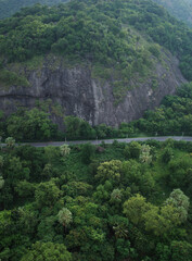 A long road cuts between huge rock mountains and green forests, road trip for holiday with nature landscape