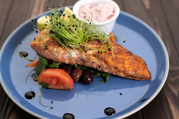 grilled salmon fillet with tomatoes and lemon on a blue plate on a wooden table