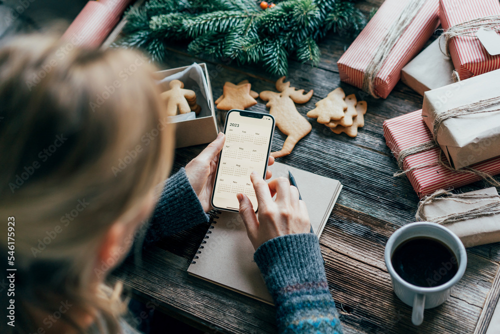 Wall mural woman planning 2023 holding a phone with a calendar on the screen working on christmas desk