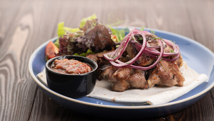 Grilled pork dish with fresh vegetables. Food foto of grilled pork cubes with onion and lettuce. Tasty cook meat with vegetables on wooden background.