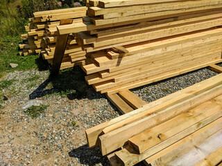 Wooden boards stacked in rows and lie on the ground. Boards for construction are sawn with bars. Close-up