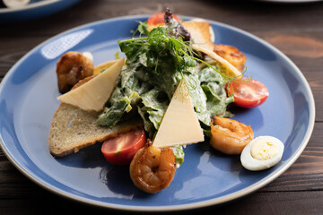 Fresh Caesar salad on blue bowl with parmesan cheese and shrimps.